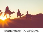 Camel caravan with people going through the sand dunes in the Sahara Desert. Morocco, Africa.