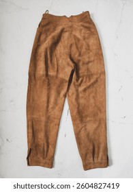 Camel real suede women's trousers back side. Brown high waisted vintage ankle length pants flat lay top view at white background. Natural genuine goat leather pants for woman. Clothes, apparel, fashio