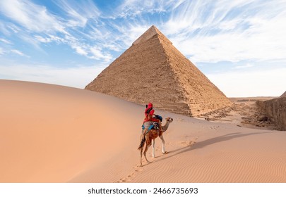 Camels in Giza Pyramid Complex - A woman in a red turban riding a camel across the thin sand dunes - Cairo, Egypt