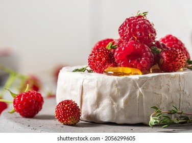 Camembert cheese with fresh raspberries, strawberries, honey and thyme on white background. French appetizer. Close up. Macro shot