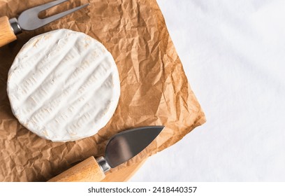 Camembert cheese, cheese knife and fork on craft paper on the table. Top view. Copy space. Close-up. Selective focus. - Powered by Shutterstock