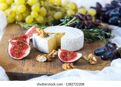 Camembert cheese, sliced ​​figs and grapes of green and blue flowers are on a dark wooden board with a sprig of rosemary and oregano. - Powered by Shutterstock