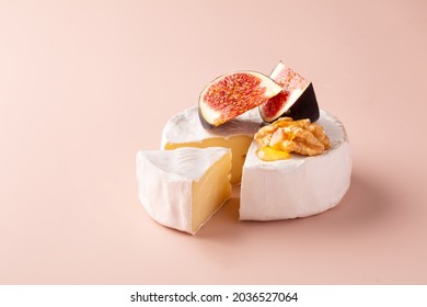 Camembert cheese with white mold, fresh figs, walnuts and honey on a pink pastel background.