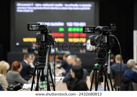 Camera during shareholders' meeting with big screen in the background