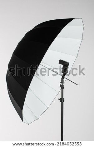 Camera flash head mounted on stand with umbrella light reflector in photography studio