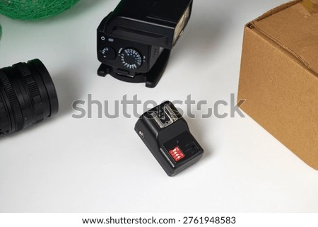 Camera flash trigger and speedlight with lens and box on white background. Studio setup for photography equipment, lighting accessories, and creative shooting tools.