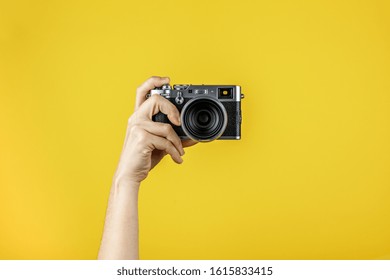 Camera held by one hand in front of a yellow background
