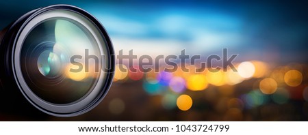 Camera lens with lense reflections on blur night city. Media and technology concept background.