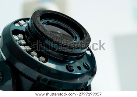 A camera lens is shown up close with various components visible. The lens sits on a flat surface in a studio. Soft light highlights the details of the lens.
