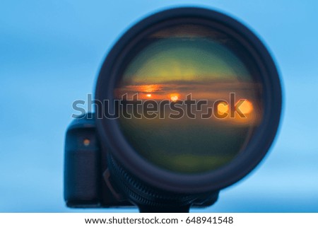 The camera lens with a sunset reflection on the background of the sky