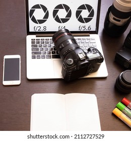 Camera lies on laptop keyboard. Photo equipment, smartphone, notebook nearby. Diaphragm drawing on the screen. Concept of online courses, photography training, photographer profession, new skills