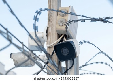 A camera is mounted on a pole next to a barbed wire fence