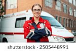 Camera moving away from Caucasian young pretty woman doctor in glasses smiling at camera standing on street near hospital. Close up of female paramedic outdoor near ambulance car. Emergency worker