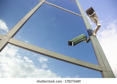 camera on glass facade of office building reflecting clouds and blue sky