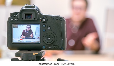 Camera On A Tripod Filming A Blogger At Home Sitting On His Workspace