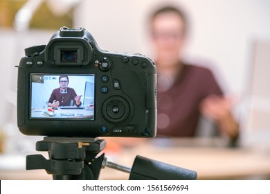 Camera On A Tripod Filming A Blogger At Home Sitting On His Workspace