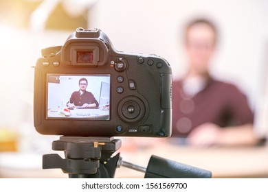 Camera On A Tripod Filming A Blogger At Home Sitting On His Workspace