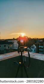 A camera on a tripod on a rooftop capturing the sunset view