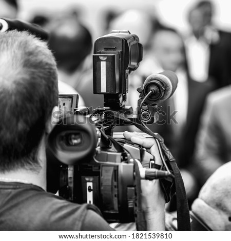 Camera operator working at a press conference outdoors. Journalists interviewing formal dressed politician or businessman at a media event. 
