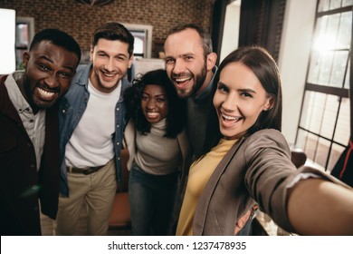 camera point of view of group of cheerful coworkers taking selfie using smartphone 