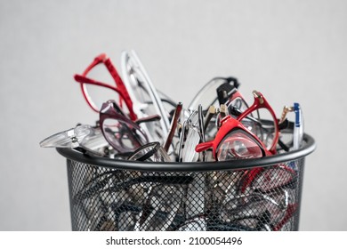 Camera Shows Pile Of Multi-colored Frame Glasses Put Into Black Trash Bin Against Grey Background As Request To Improve Eyesight Closeup