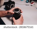 Camera technician inspecting an interchangeable camera lens mount and electronic contacts at a technical service workbench