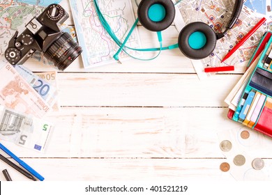 Camera, Touristic Maps, Headphones, Wallet With Credit Cards, Phone, Colorful Pens, Euro Banknotes And Coins On The White Desk. Travel Background. Journey Planning. Tourist Essentials. Space For Text