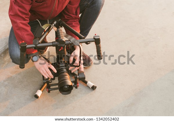 Cameraman adjusts the dskr camera to the\
stabilizer. Stabilizer is on the ground. Man is a videographer and\
a mirrorless camera with a stabilizer. Preparation for\
shooting.Backstage.\
Copyspace
