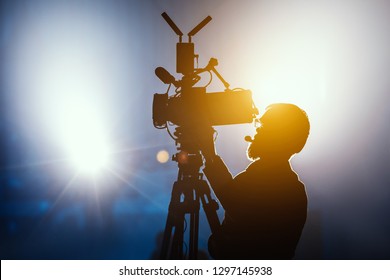 Cameraman silhouette on a live studio news stage.Professional cameraman with headphones with camcorder in television news broadcast.