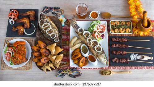 Cameroon specialty assortment. Tilapia fish, samosa and ndole, chicken and goat meal, manioc and vegetable, plantain and shrimp. Served on wooden table with different spices and tropical decoration.
