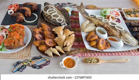 Cameroon specialty assortment. Tilapia fish, samosa and ndole, chicken and goat meal, manioc and vegetable, plantain and shrimp. Served on wooden table with different spices and tropical decoration.