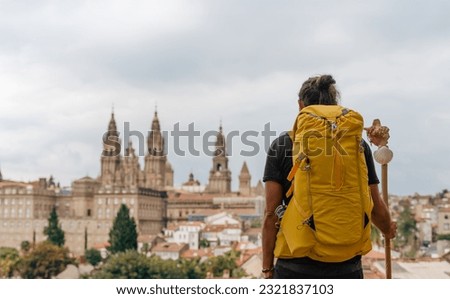 Camino de Santiago - Young hipster pilgrim ends the Way of St James pilgrimage enjoying cathedral and the Santiago de Compostela old town cityscape in Galicia, Spain