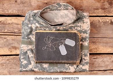 Camouflage army clothes, book, and dog tags on wood. Flay lay, top view.