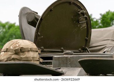 Camouflage helmet on the open hatch of a military vehicle. Greenery and tarp in the background.