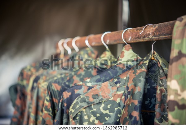 Camouflage military jackets hanging on a rusty\
clothing rack