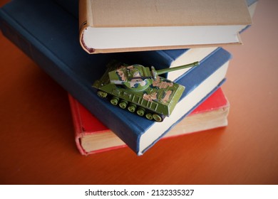 Camouflage Toy Tank Stacked On Old War Books On Brown Wooden Table