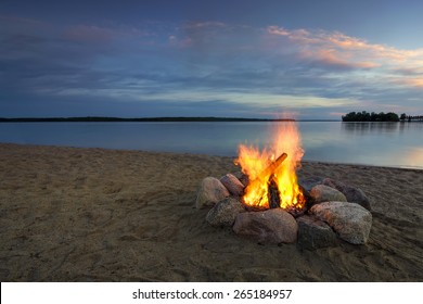 Camp fire on sandy beach, beside lake at sunset. Minnesota, USA