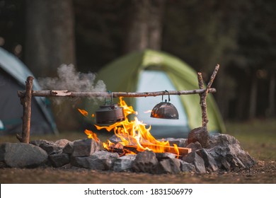 Camp fire and tea pot are foreground and focused, there is a tent in the background and defocused - Shutterstock ID 1831506979