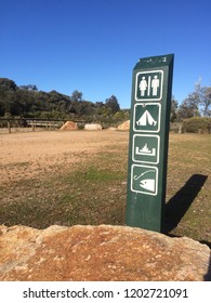 Camp Ground Sign Post With A Rock, Vegetation And Sand Dunes In The Background. Toilets, Camping, Campfire And Fishing Allowed Wooden Green Painted Sign The Ninety Mile Beach, East Gippsland, Victoria