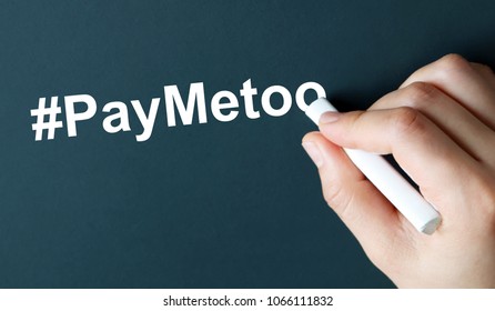 The hand writing text #PayMeToo in white chalk. A Campaign To Close The Gender Pay Gap.