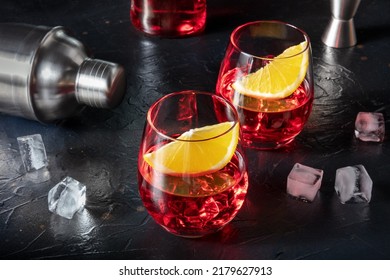 Campari Aperitif Garnished With Fresh Oranges, With A Cocktail Shaker, Ice Cubes, And A Jigger And A Bottle In The Background