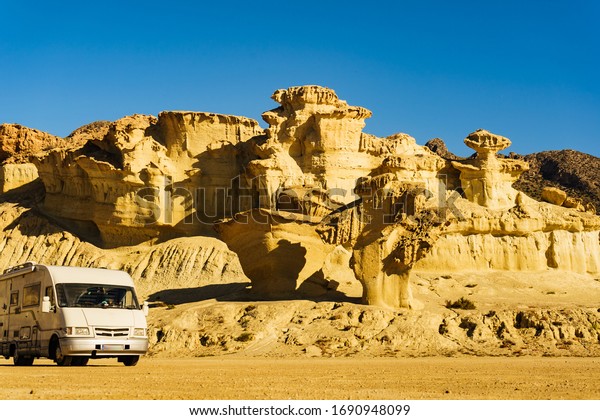 Camper car on parking area at eroded yellow\
sandstone formations, Enchanted City of Bolnuevo, Murcia Spain.\
Tourist attraction.