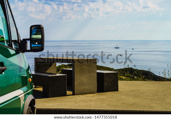 Camper car on rest stop area, viewpoint with\
stone seating bench on sea ocean shore. Attractions along Lofoten\
islands in Norway.