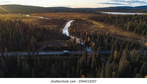 Camper van in a autumn forest in Lappland, aerial drone view of a caravan car, driving in middle of foliage trees, on a sunny fall evening, in Lapland