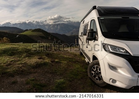 camper van parked on green meadow with a background of snowy mountains in the morning after sleeping