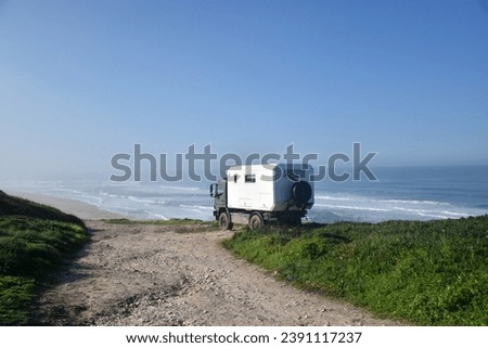 camper van parked on the side of a cliff with the beach in the background