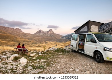 Camper van parked with people sitting looking on over the mountains in the Durmitor National Park in Montenegro at sunset