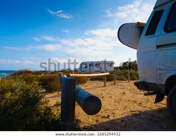 Camper van with surf board camping on\
beach sea shore. Holidays, sport and adventure\
concept.
