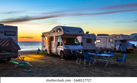 Campers and Motorhomes overlooking sunset in the Mediterranean sea from their campsite on the beach, Corsica, France