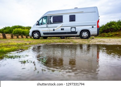 Campervan Or Motorhome Camping On Rainy Day With Rain Puddles. Family Vacation Road Trip With Camper Van, Motor Home Or RV In With Bad Weather. Holiday Travelling To Atlantic Ocean - Spain Or Portugal